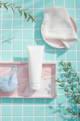 White tube and soft towel placed on a marbled tray with round dish beside. Botanical branches frame...