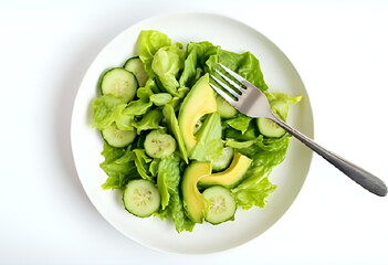 Flatlay of fresh green salad with lettuce, cucumber, and avocado slices, served on white ceramic plate with stainless fork. Clean background, bright natural light, minimal and healthy.