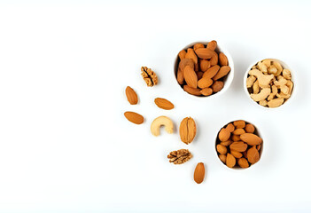 Flatlay of assorted nuts (almonds, cashews, walnuts) arranged in small ceramic bowls on white background. Clean minimal composition with copy space for packaging or health themes.