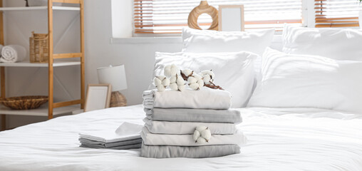 Stack of clean bed sheets with cotton flowers in bedroom