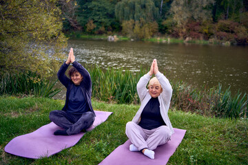 middle-aged woman teaches her old mother somatic exercises and yoga to maintain health by the river...