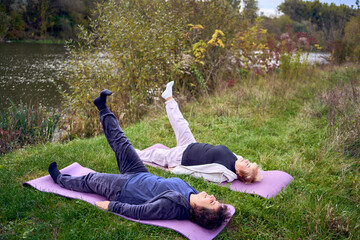 middle-aged woman teaches her old mother somatic exercises and yoga to maintain health by the river in autumn