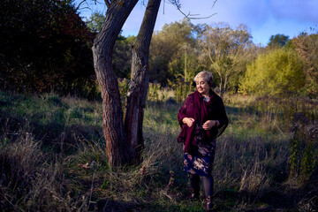 portrait of an elderly woman with gray hair in a dress and shawl in the autumn forest