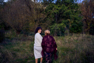 middle-aged daughter and elderly mother together on a walk in the autumn forest