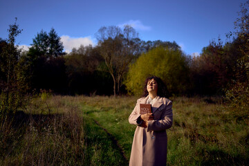 a middle-aged woman in a beige coat with a holy bible in her hands prays for peace in the autumn...