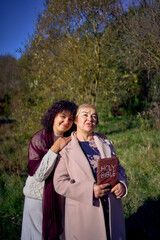 middle-aged woman and elderly mother with holy bible in hands praying for peace in autumn forest