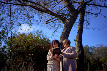 middle-aged woman and elderly mother with holy bible in hands praying for peace in autumn forest