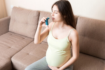 pregnant woman using asthma inhaler during attack for being healthy on sofa at the home. Healthy...