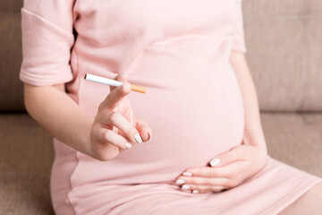 Close-up of pregnant woman is holding a cigarette sitting on sofa at home