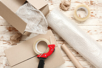 Packing tape dispenser, cardboard boxes and roll of bubble wrap on wooden background