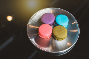 Typical French sweets. four contemporary flavours of macarons in round stainless steel plate on a black glass table in a cafe dessert shop.