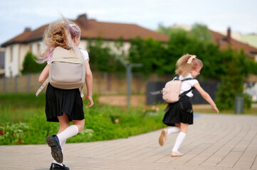 schoolgirls with backpacks running joyfully on pathway, wearing uniforms and white socks, heading...