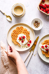 Frische Waffeln mit Joghurt und Himbeeren auf zwei Teller. Weiblilche Hand, Frühstück, Draufsicht.