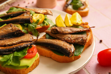 Plate of tasty sandwiches with canned smoked sprats on table