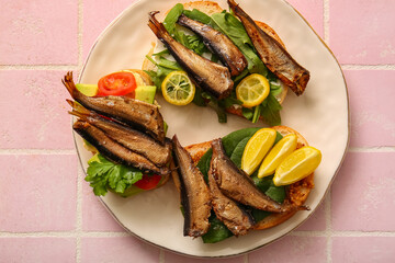 Plate of tasty sandwiches with canned smoked sprats on pink tile background