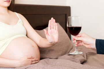 Close up of pregnant woman staying in bed refuses to drink wine and makes stop gesture to the...