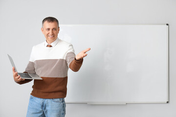 Male teacher with laptop near flipboard in classroom