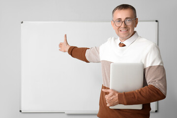 Male teacher with laptop pointing at flipboard in classroom