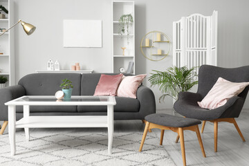 Interior of light living room with grey armchair, footstool and sofa