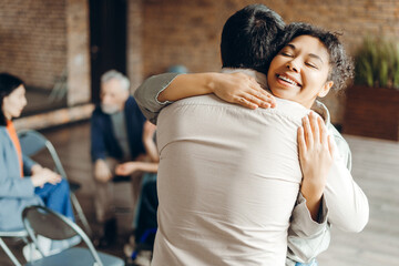 Happy African American woman psychologist hugging man at support group meeting