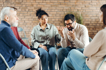 Group of sad patients, talking with psychologist during therapy session