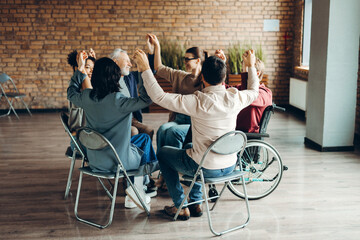 Diverse multinational group holding hands together sitting in modern office
