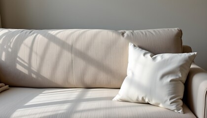an interior setting featuring a beige upholstered sofa against a light colored wall with a window allowing natural light to enter