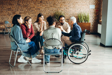Diverse group of people supporting senior man in wheelchair during therapy session