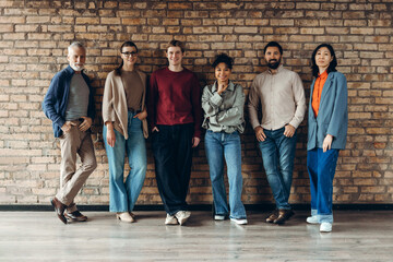 Group of diverse multinational team posing by brick wall: colleagues collaboration and innovation