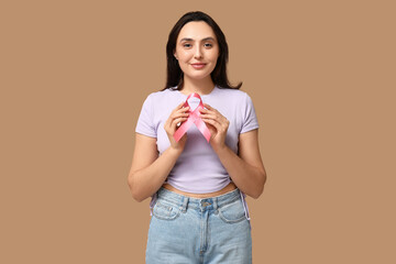 Pretty young woman with pink ribbon on beige background. Breast cancer awareness concept