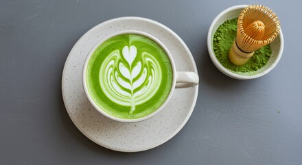 Matcha latte with latte art and whisk on a gray table