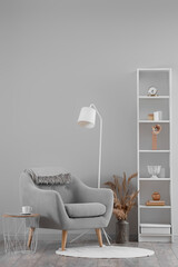 Interior of living room with armchair,  lamp and shelves with decoration near grey wall