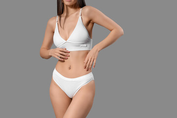 Slim young woman in white cotton underwear on grey background