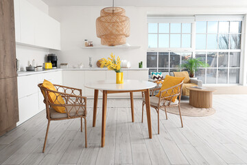 Interior of cozy stylish kitchen studio with table, armchairs, mimosa flowers, houseplant, counters and sofa