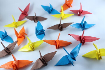 A colorful array of red, orange, yellow, blue, and brown origami cranes scattered across a clean...