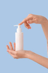 Female hands with bottle of cream on color background, closeup