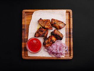 Delicious grilled meat served with onions and spicy sauce on a wooden platter