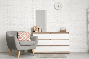 Armchair and chest of drawers with mirror near white brick wall in living room