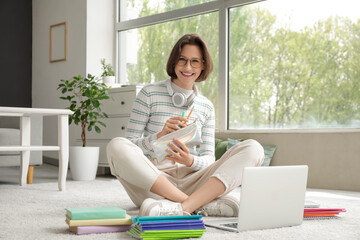 Beautiful student with pencil case studying on floor at home