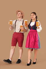 Young happy couple in traditional German clothes with glasses and mugs of beer on beige background