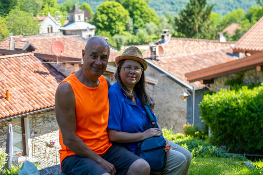 Tourist Hiking mature couple enjoys leisurely walk along Province Verbano-Cusio-Ossola region Piedmont, sitting on bench and resting Italian Montorfano historic village