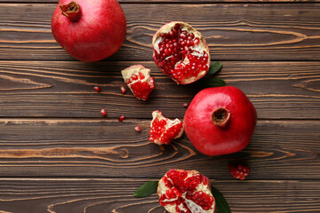 Fresh ripe pomegranates with seeds and leaves on wooden background