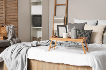Tray with kettle, cup and frame on bed in bedroom