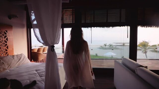 Woman in a sheer white robe walks through a luxury villa overlooking a beach sunrise in Mexico