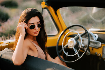 Stunning woman in sunglasses enjoys a classic convertible car in a scenic location during sunset