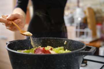 A person is adding spices to a pot filled with chopped vegetables and meat