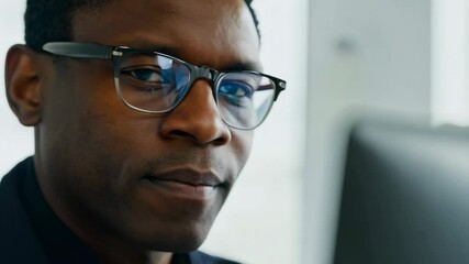 Close-up video of a middle aged African American man in front of laptop monitor in office. The man’s serious look conveys his dedication, fully immersed in his work on the laptop. - Powered by Adobe
