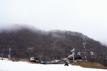 Obraz premium Hakuba Goryu Snow Resort is a popular ski resort located in the Hakuba Valley, Nagano.Winter Sports Park at the top of the mountain snowy slope, patches of brown grass in late autumn Several ski lift.