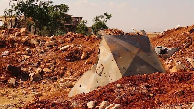 A pierced water tank lies in a dirt crater caused by a shell in rural Aleppo, Syria. . The scene marks the aftermath of a brutal war, reflecting destruction, survival, and post-conflict landscapes.