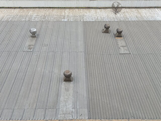 A top-down view of a corrugated metal factory roof with multiple ventilation turbines and an old...